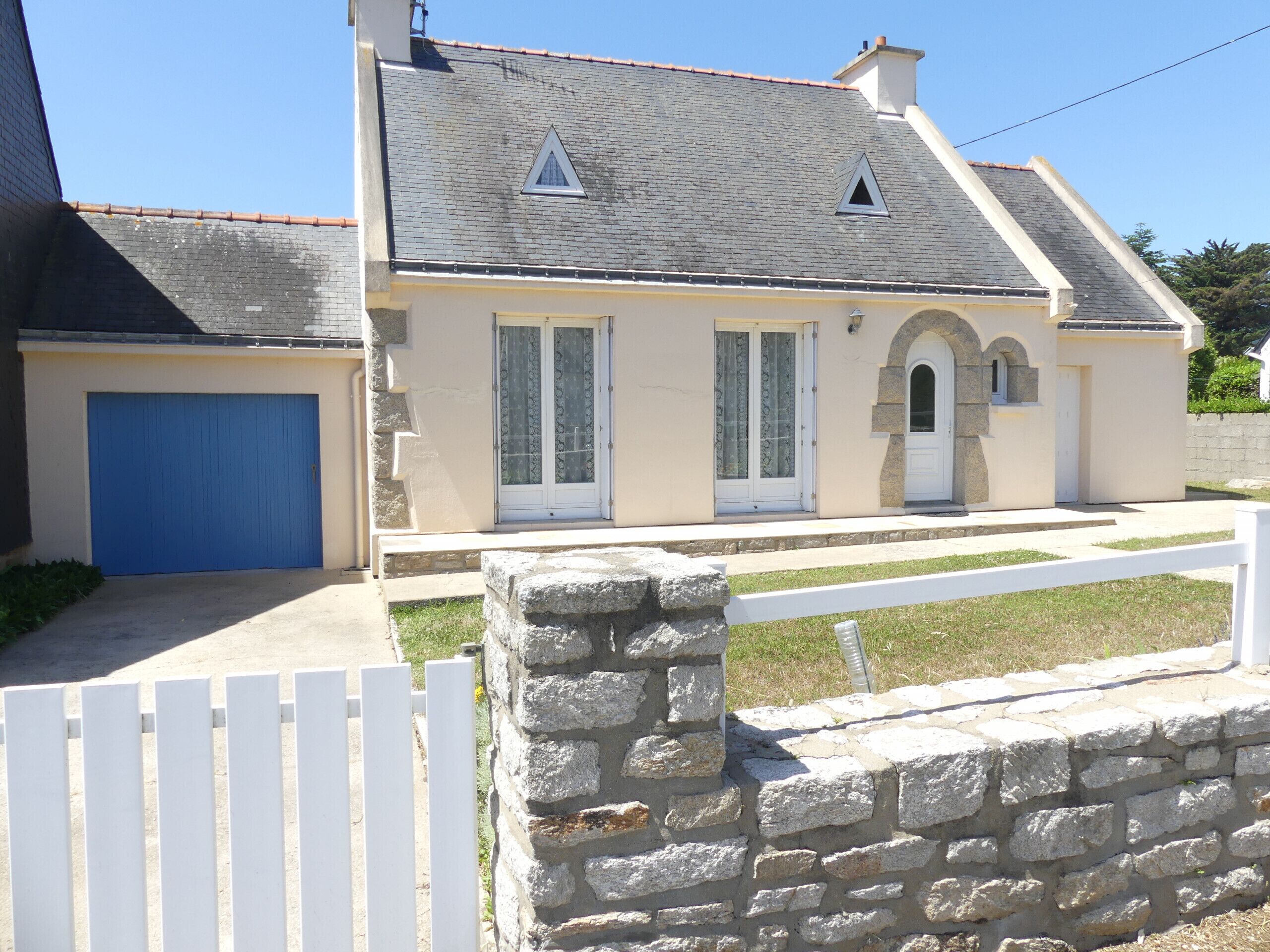 A two-story house with a blue garage door, a stone wall in front, and a white picket fence.