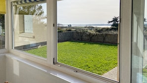 Una habitación con un ventanal grande que da a un patio césped y una vista distante de una masa de agua.