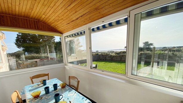 Un porche cubierto con una mesa para dos, ventanas amplias y vistas a un espacio con césped.