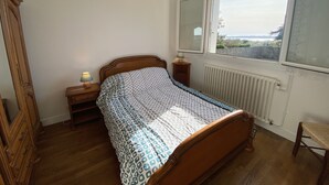 Un dormitorio con cama de madera, una mesita de noche con lámpara, una ventana con vistas y un radiador.