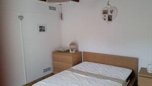 Een slaapkamer met een bed, een houten dressoir, een nachtkastje en een wandplank met een lantaarn en een ingelijst foto.