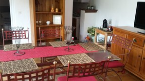 Een eethoek met een glazen tafel, rode fauteuils met kussens en decoratieve placemats.