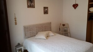 Een net opgemaakt bed met een gestructureerd hoofdbord, een klein nachtkastje en een wandplank met een decoratie in de vorm van een hart.