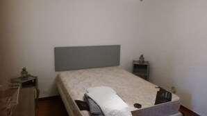 Een kleine, eenvoudige slaapkamer met een enkel bed, een nachtkastje en een dressoir.
