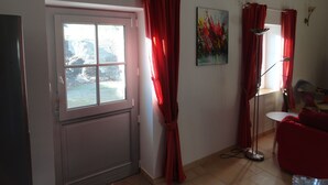 Una habitación con un ventanal grande, cortinas rojas, un cuadro en la pared y una lámpara de pie.