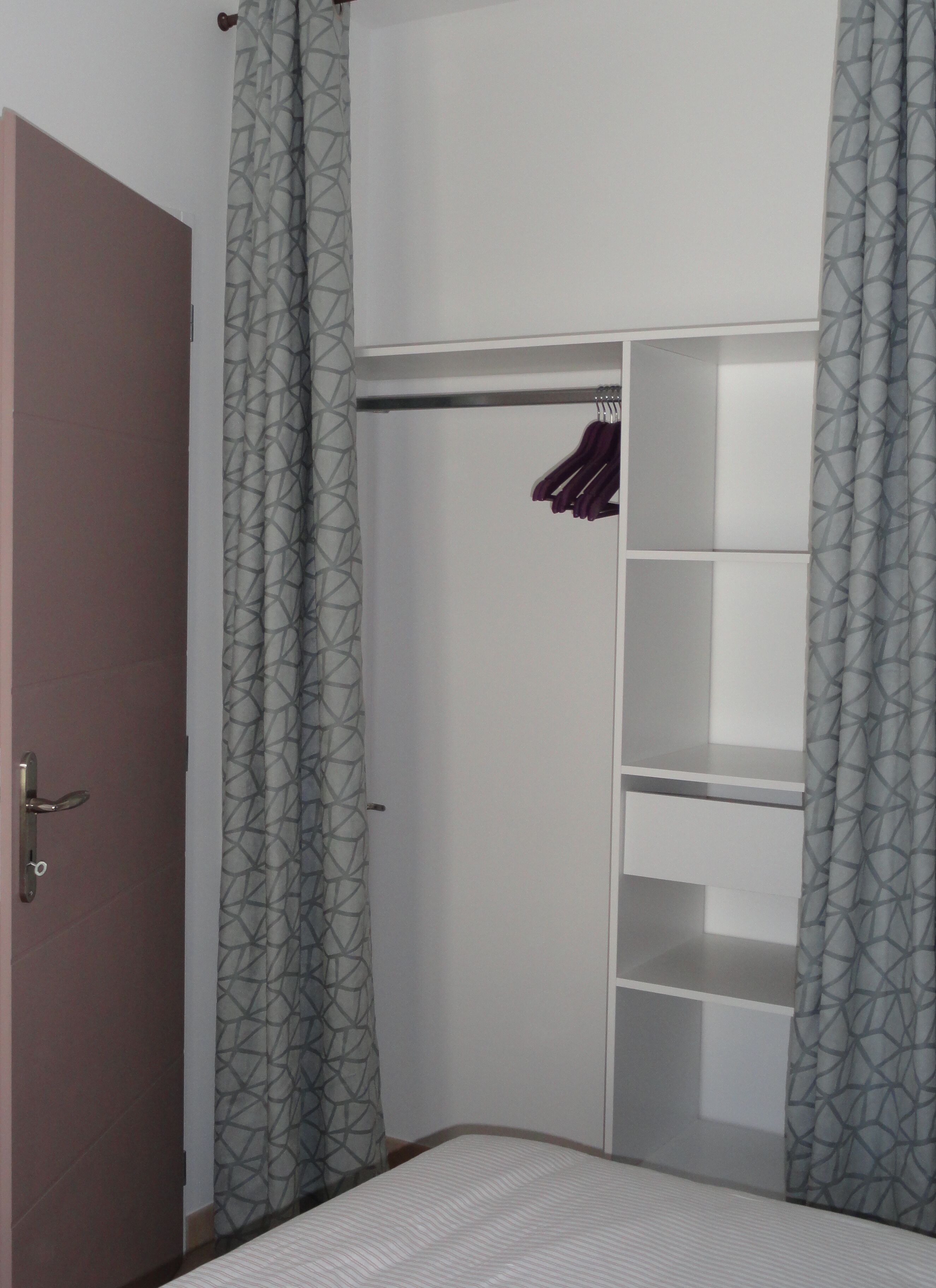 Une chambre à coucher comprenant un lit, une armoire avec espace pour suspendre les vêtements et une porte.