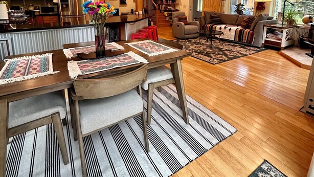 Amplia sala de estar con piso de madera, una mesa de comedor con individuales, un sofá y una estantería.