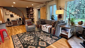 Amplia sala de estar con piso de madera, un sofá grande, una mesa de centro y una escalera que conduce a otro nivel.