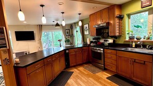 Una cocina moderna con armarios de madera, una isla central, electrodomésticos de acero inoxidable e iluminación colgante.