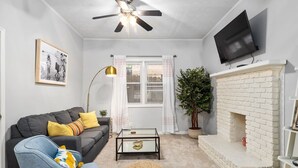 A living room with a sofa, coffee table, ottoman, fireplace, television, ceiling fan, and a framed picture on the wall. - Midtown Guest House - private entrance (Atlanta)