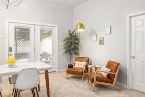 Un coin repas avec une table blanche, deux chaises, une plante et un luminaire suspendu doré.