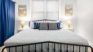 A bed with a headboard, two bedside tables with lamps, a window with blinds, and a blue curtain. - Midtown Guest House - private entrance (Atlanta)