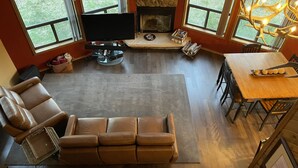 A spacious living room with a large leather sofa, a flat-screen TV, a fireplace, and a dining area with a wooden table and chairs. - Cabin in the pines (Munds Park)
