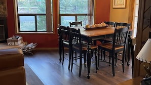 A dining area with a wooden table and chairs, a chandelier, and large windows with a view of trees. - Cabin in the pines (Munds Park)