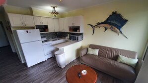 A compact kitchen with white cabinets, a refrigerator, stove, and microwave. There's a brown sofa with cushions and a small wooden table with a remote control. - Newly renovated with the lowest rates you can find. (Hilton Head Island)
