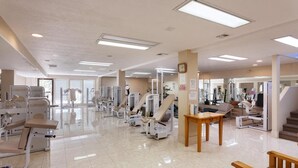 Un gimnasio espacioso con diversas máquinas de ejercicio, un reloj en la pared y un ambiente limpio y bien iluminado.