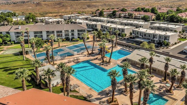 Un resort con varias piscinas, palmeras y montañas al fondo.
