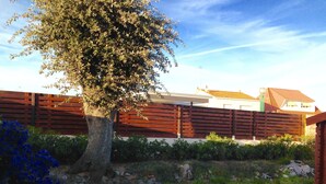 Un jardin clos avec un arbre, un mur de pierre et, au fond, un bâtiment doté d’un toit en tuiles.