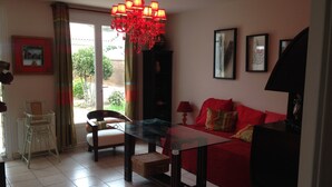 Un salon avec un canapé rouge, une table basse en verre, une table à manger et un lustre rouge.