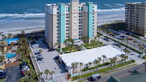 A multi-story hotel with a pool and beach view, located near a beach with a parking lot and street.