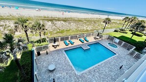 A rooftop pool with lounge chairs, a small circular seating area, and a view of the beach and ocean.