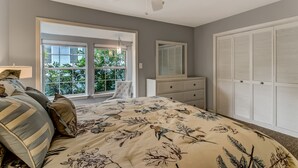 Une chambre à coucher comprenant un lit, une commode, un ventilateur de plafond et une fenêtre donnant sur un paysage verdoyant.