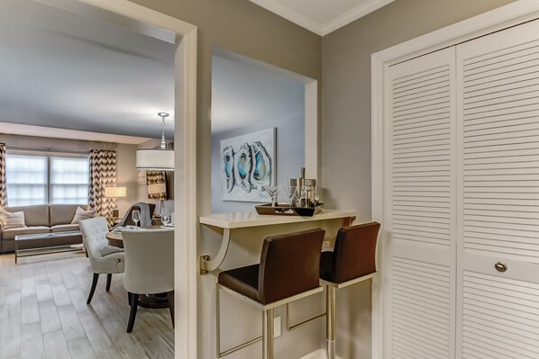 A modern living room with a sofa, dining table, and chairs. There is a painting on the wall and a white closet with a door.