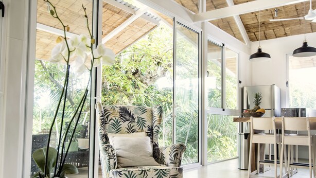 Una habitación amplia con un gran ventanal, un sillón estampado, un comedor y una cocina con refrigerador.
