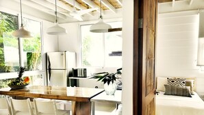 Una cocina moderna con electrodomésticos blancos, encimera de madera y una zona de comedor con sillas blancas.