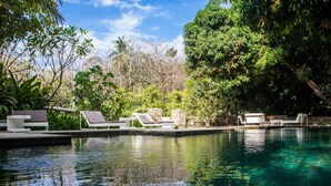 Una piscina cristalina con sillas de descanso y un muro de piedra.