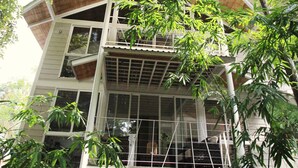 Un edificio de varios pisos con amplios ventanales y un nivel superior de madera, rodeado de abundante follaje.