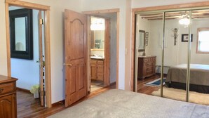 Une chambre à coucher avec un lit, une armoire en bois et une salle de bain visible à travers une porte ouverte.