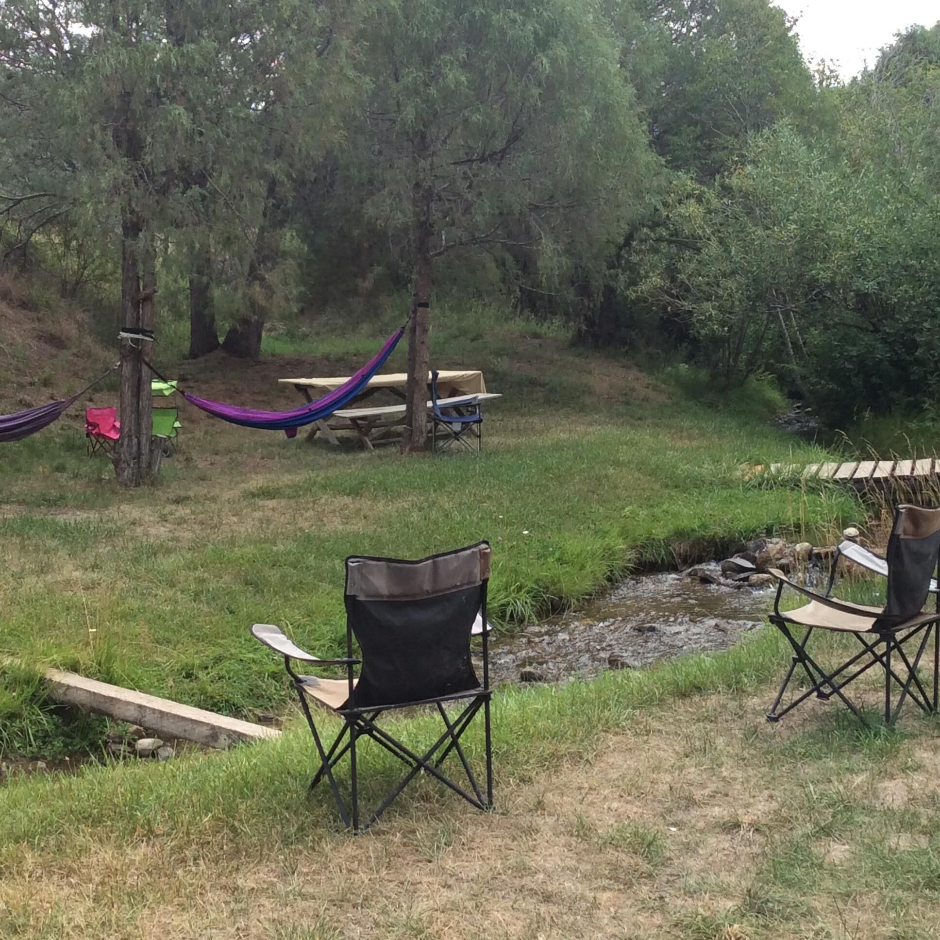 A grassy outdoor area with picnic tables, a hammock, and folding chairs.