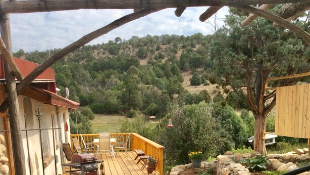 Une terrasse en bois avec des meubles d’extérieur, un mur en pierre et une vue sur un paysage vallonné.