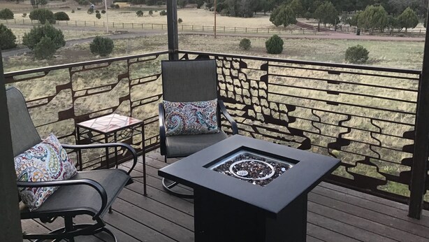 Terraza con dos sillas y una mesa, con vista a un campo cubierto de hierba y árboles.