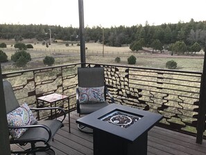 A deck with two chairs and a table, overlooking a grassy field and trees.