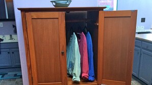 Un armario de madera con las puertas abiertas, mostrando ropa colgada.