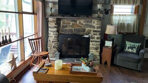 Un salon chaleureux avec une cheminée en pierre, un téléviseur fixé au-dessus, et un coin salon confortable avec un fauteuil et un canapé.
