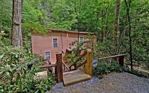 A rustic cabin with a wooden deck and a staircase leading up to a door. - 1,000 Ft Creekfront | Hot Tub, Fire Pit, Games, Direct Trail Access & Dogs OK (Cherry Log)