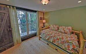 Une chambre avec une grande fenêtre, un lit recouvert d’une literie à motifs floraux, une tête de lit en bois et une lampe de chevet.
