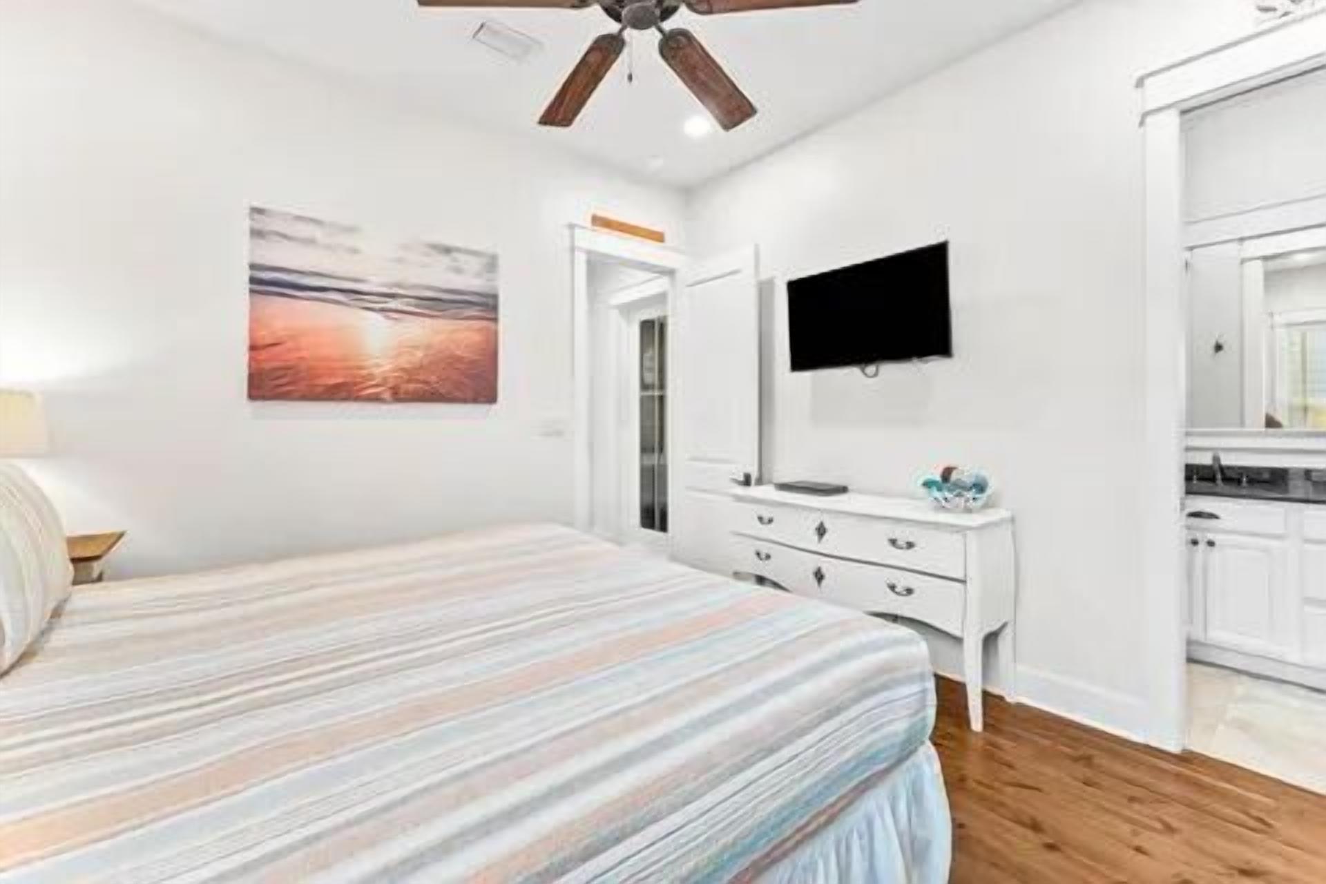 Un dormitorio con cama, cómoda, televisor montado en la pared y puerta que da a un baño.