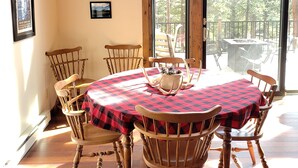 Un comedor con una gran mesa cubierta por un mantel a cuadros, rodeada de sillas de madera. Encima de la mesa, una araña de techo con cuernos de ciervo, y cuadros en la pared.