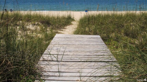 Un camí de fusta que porta a una platja amb aigua blava i cristal·lina.