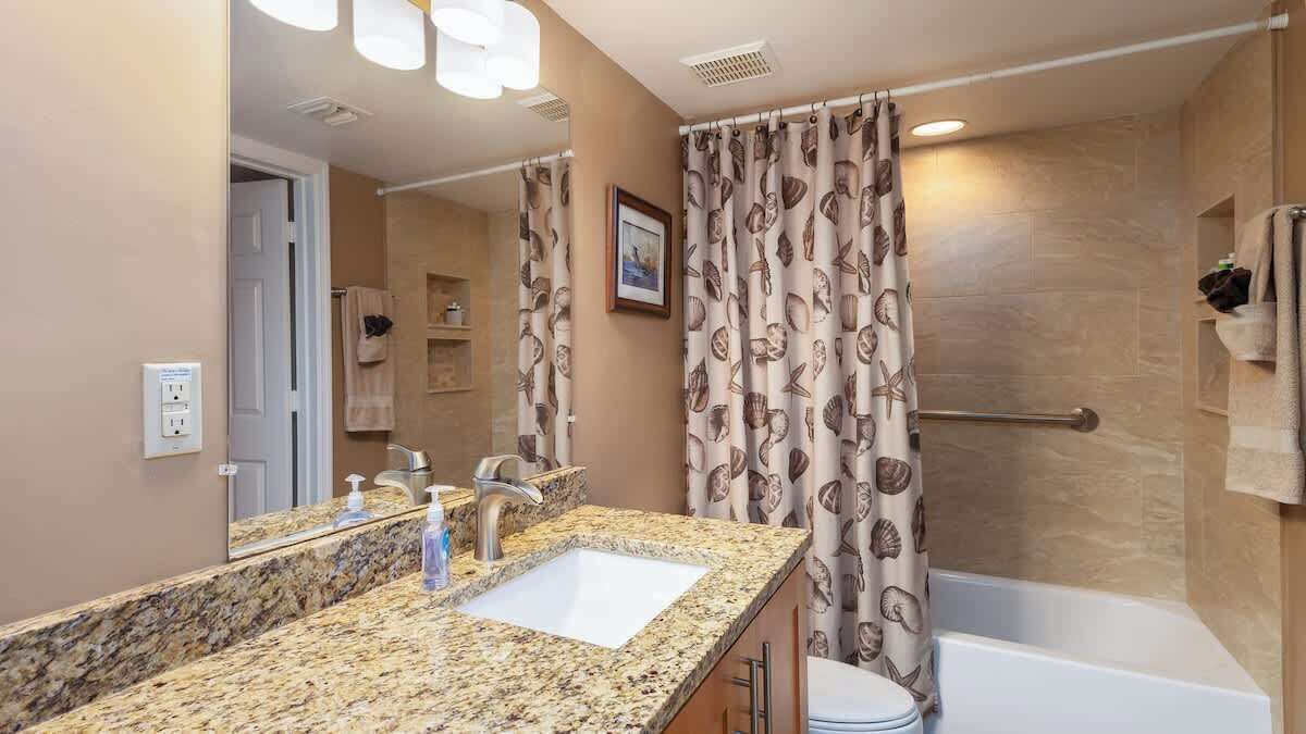 A bathroom with a granite countertop sink, a bathtub, and a shower curtain with a shell pattern.