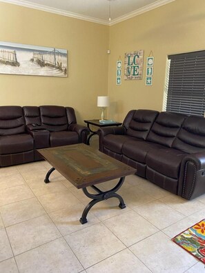 A living room with two brown leather sofas, a wooden coffee table, a small side table with a lamp, and a colorful rug.