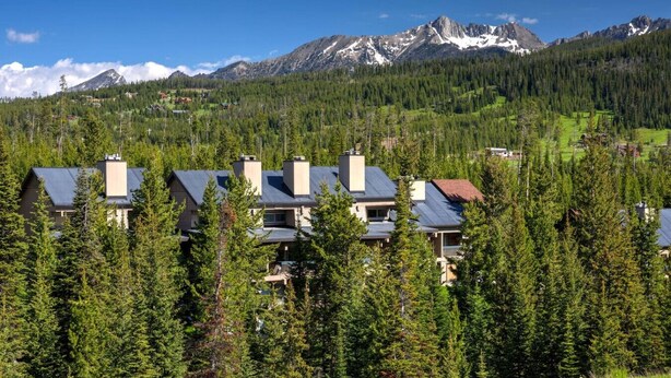 A residential area with multiple houses surrounded by dense forest and mountains in the background. - Cozy Slope-Side 2 Bedroom, Walk to Chairlifts! (Big Sky)