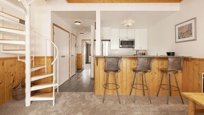A kitchen with a wooden island, bar stools, and a staircase. - Cozy Slope-Side 2 Bedroom, Walk to Chairlifts! (Big Sky)
