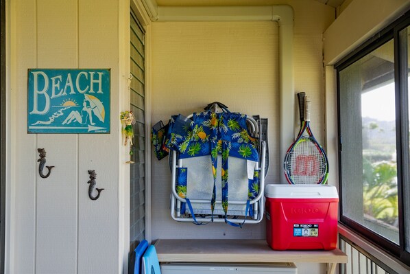 A room with a 'Beach' sign, a towel rack with a towel, a red cooler, and a tennis racket.