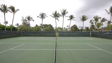 A tennis court with multiple courts, surrounded by palm trees and a fence.