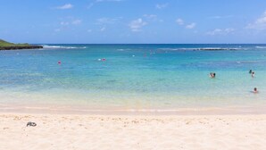 A beach with clear turquoise water, a sandy shore, and a few people swimming.